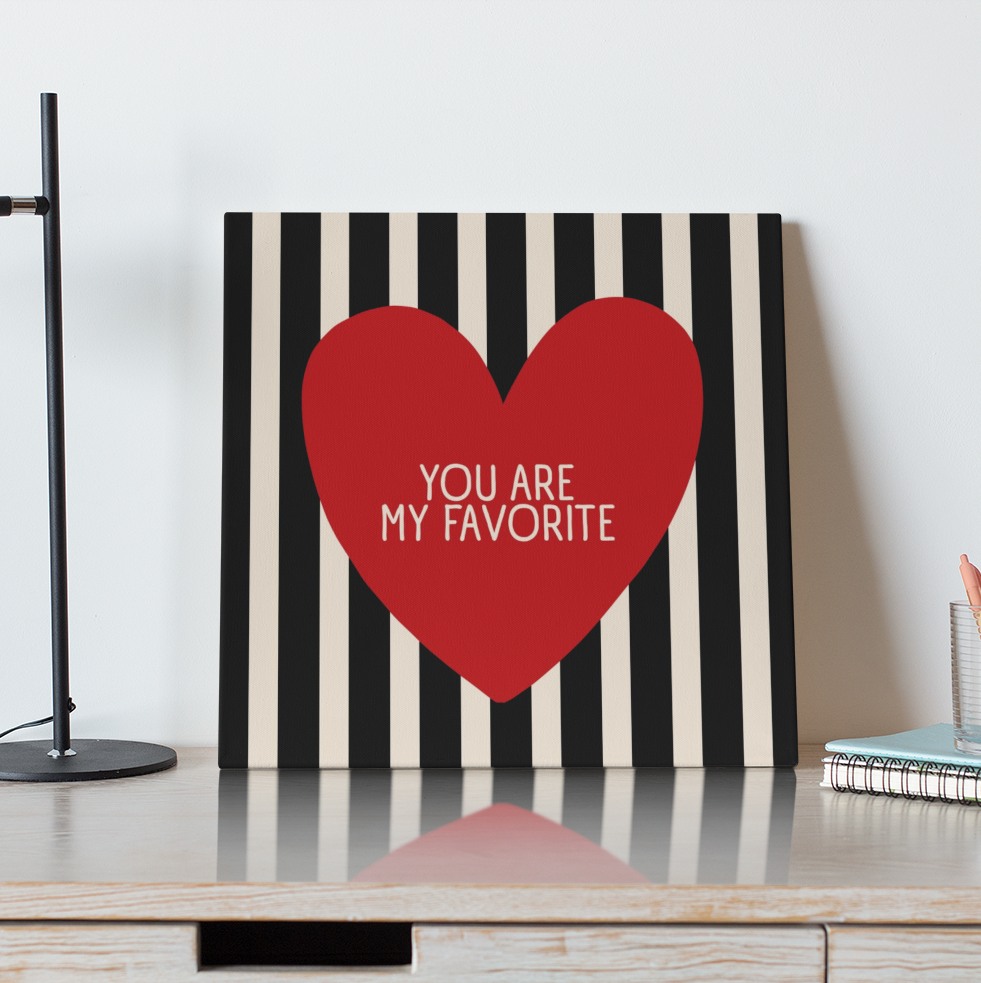 Decorative wall art with a red heart and text on a striped background, placed on a wooden surface.