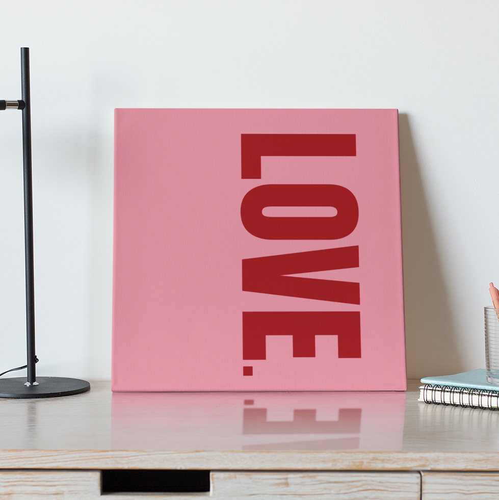 Pink 'LOVE' sign on a wooden desk with a black lamp and coffee cup.